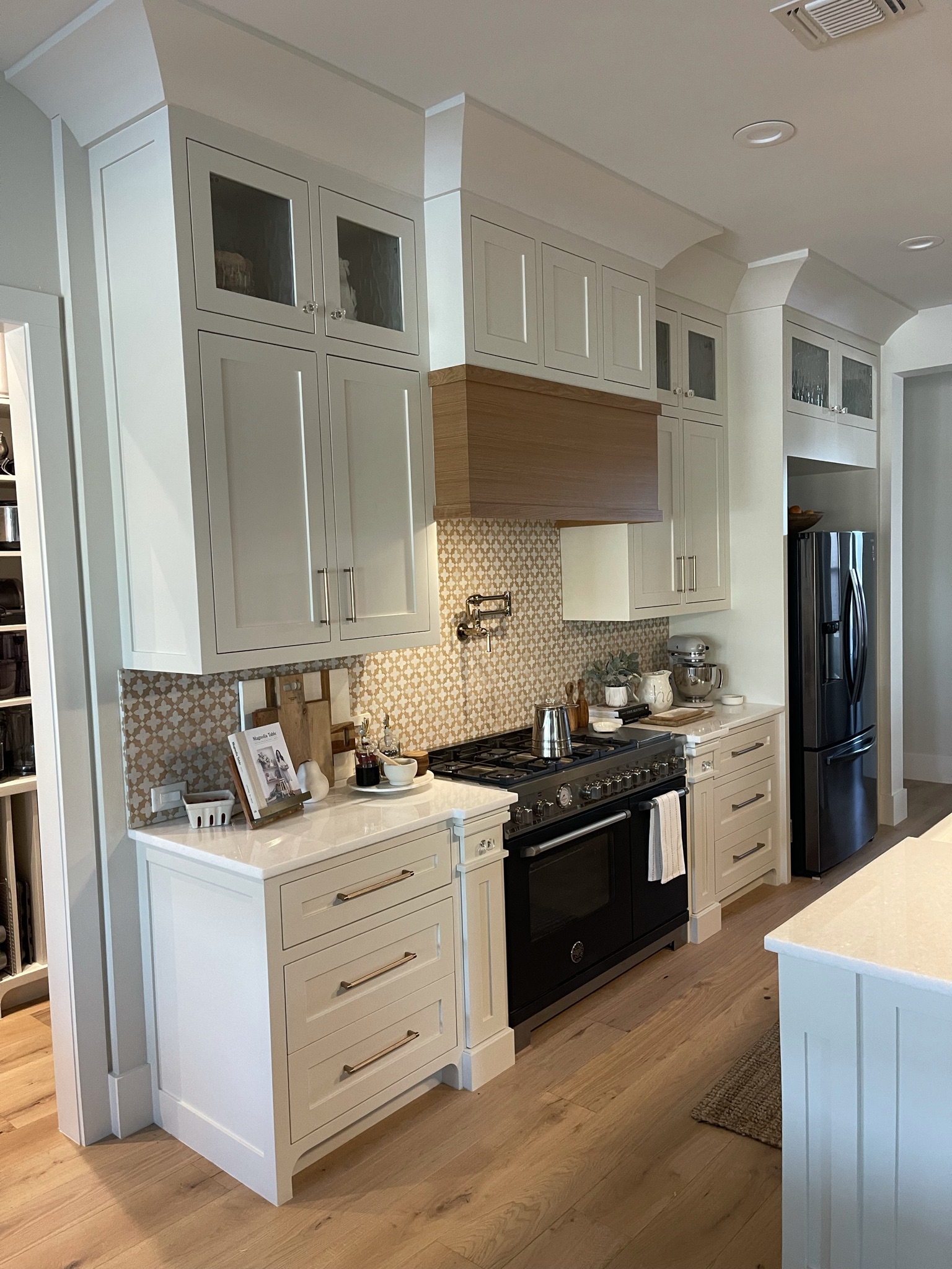 Modern Farmhouse Kitchen Cabinetry with Silver Pulls with Wooden Range Hood Above Oven.